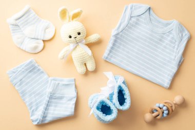 Baby shower concept. Top view photo of blue shirt pants knitted bunny toy tiny shoes socks and wooden rattle on isolated pastel beige background