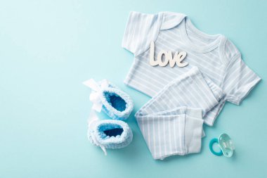 Baby shower concept. Top view photo of infant clothes blue shirt pants inscription love knitted booties and pacifier on isolated pastel blue background