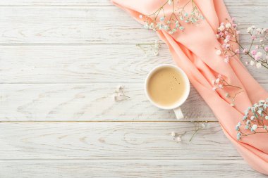 Hello spring concept. Top view photo of cup of frothy coffee gypsophila flowers and pink scarf on grey wooden desk background with blank space