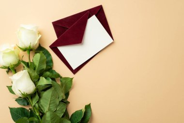 Saint Valentine's Day concept. Top view photo of red envelopes with letter and bouquet of white roses on isolated beige background with empty space