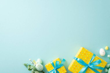 Easter decorations concept. Top view photo of yellow present boxes with blue ribbon bows and bouquet with easter eggs on isolated pastel blue background with copyspace