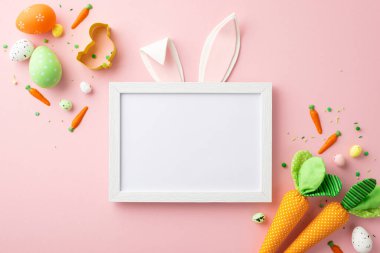 Easter decor concept. Top view photo of photo frame with easter bunny ears colorful eggs carrots baking mold and sprinkles on isolated pastel pink background with blank space