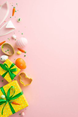 Easter concept. Top view vertical photo of easter bunny ears eggs yellow gift boxes baking molds and carrot shaped sprinkles on isolated pastel pink background with copyspace