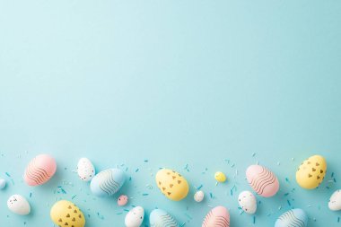 Top view photo of easter decorations yellow pink blue white eggs and sprinkles on isolated light blue background with copyspace