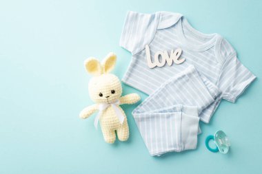 Baby shower concept. Top view photo of infant clothes blue shirt pants inscription love knitted bunny toy and pacifier on isolated pastel blue background