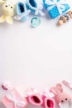 Baby concept. Top view vertical photo of pink and blue knitted booties gift boxes bunny toys wooden rattle and pacifiers on isolated white background with copyspace