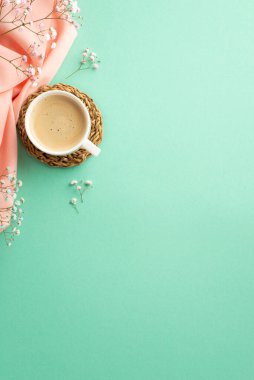 Hello spring concept. Top view vertical photo of cup of frothy coffee on rattan serving mat gypsophila flowers and pink soft plaid on isolated teal background with copyspace