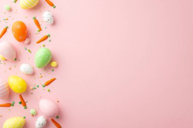 Easter celebration concept. Top view photo of orange green yellow easter eggs small carrots and sprinkles on isolated light pink background with empty space