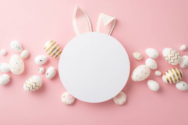 Easter concept. Top view photo of easter bunny ears and paws on white circle white and golden eggs on isolated pastel pink background with blank space