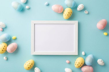 Easter party concept. Top view photo of empty photo frame and colorful easter eggs on isolated pastel blue background with copyspace