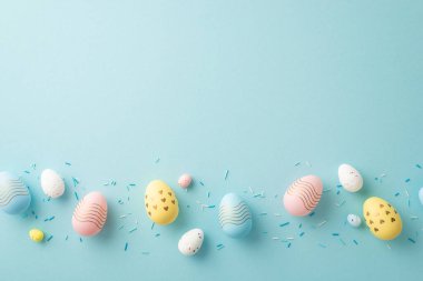 Easter concept. Top view photo of colorful easter eggs in row and sprinkles on isolated pastel blue background with copyspace