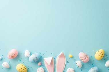 Easter concept. Top view photo of easter bunny ears colorful eggs and sprinkles on isolated light blue background with copyspace