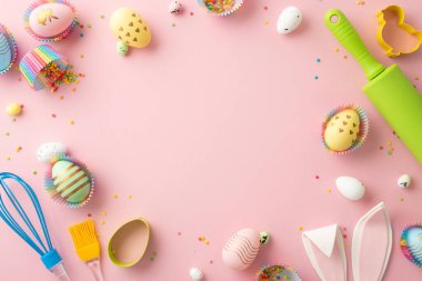 Easter concept. Top view photo of kitchen utensils colorful easter eggs in paper baking molds bunny ears and sprinkles on isolated pastel pink background with empty space in the middle