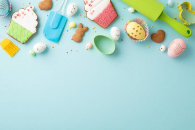 Top view photo of rolling-pin silicone spatula brush colorful easter eggs in paper baking molds cake shaped gingerbread cookies and sprinkles on isolated pastel blue background with empty space