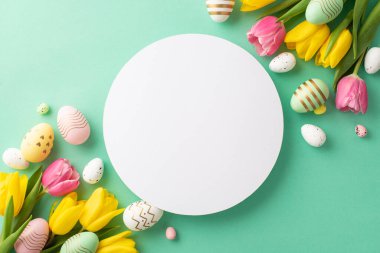 Easter concept. Top view photo of white circle colorful easter eggs and bunches of yellow and pink tulips on isolated teal background with copyspace