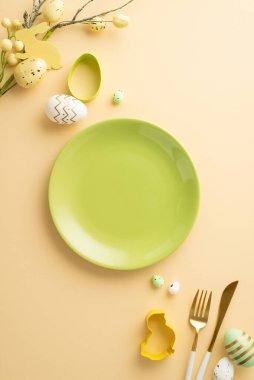 Easter celebration concept. Top view vertical photo of empty green plate easter eggs cutlery baking molds and easter bouquet on isolated pastel beige background