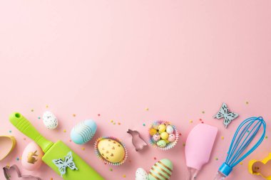 Easter concept. Top view photo of kitchen utensils whisk rolling pin silicone spatula colorful easter eggs in paper baking molds butterflies sprinkles on isolated pastel pink background with copyspace