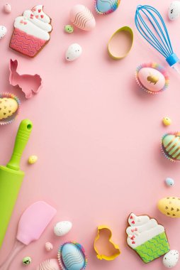 Easter concept. Top view vertical photo of rolling pin silicone spatula whisk colorful easter eggs in paper baking molds and gingerbread on isolated pastel pink background with copyspace in the middle