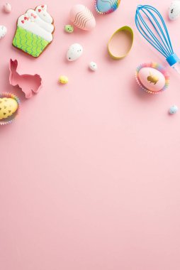 Easter concept. Top view vertical photo of whisk colorful easter eggs in paper baking molds and cupcake shaped gingerbread on isolated pastel pink background with empty space