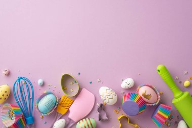 Easter cooking concept. Top view photo of kitchen utensils whisk rolling pin silicone spatula brush colorful easter eggs in paper baking molds and sprinkles on isolated lilac background with copyspace