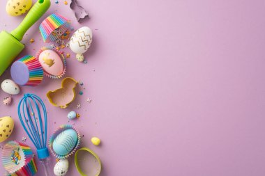 Easter cooking concept. Top view photo of kitchen utensils whisk rolling pin colorful easter eggs and paper baking molds with sprinkles on isolated pastel violet background with copyspace