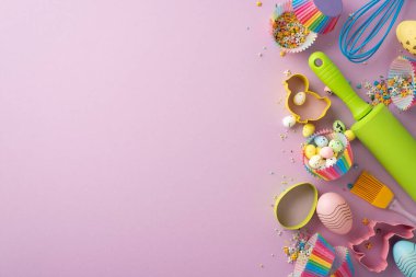 Easter celebration concept. Top view photo of kitchen utensils whisk rolling pin brush colorful easter eggs and paper baking molds with sprinkles on isolated lilac background with empty space