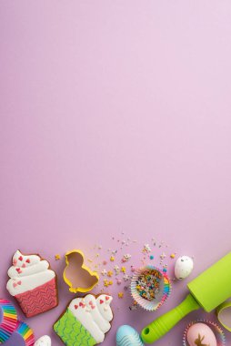 Easter concept. Top view vertical photo of easter eggs cupcake shaped gingerbread rolling-pin and baking molds with sprinkles on isolated lilac background with copyspace