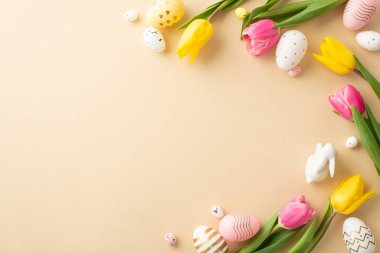 Easter decorations concept. Top view photo of colorful easter eggs ceramic easter bunny and tulips on isolated light beige background with empty space