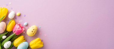 Easter decorations concept. Top view photo of bouquet of yellow and pink tulips colorful easter eggs and confetti on isolated lilac background with empty space