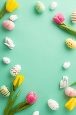Easter celebration concept. Top view vertical photo of ceramic easter bunnies tulips and colorful easter eggs on isolated teal background with copyspace in the middle