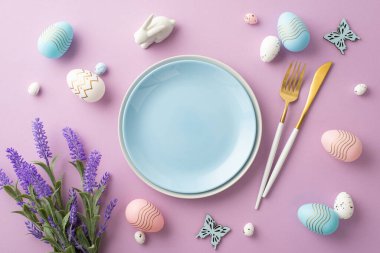 Easter celebration concept. Top view photo of empty blue plate cutlery pink blue white easter eggs ceramic bunny butterflies and bouquet of lavender flowers on isolated lilac background