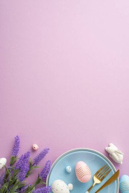 Easter concept. Top view vertical photo of blue dish knife fork colorful easter eggs ceramic bunny and lavender flowers on isolated lilac background with copyspace