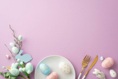 Paskalya konsepti. Üst görüntüde mavi beyaz yumurta çatal bıçak dekoru ve izole edilmiş eflatun arkaplanlı seramik tavşan resmi var.