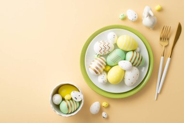 Paskalya kutlaması. Sarı yeşil paskalya yumurtası çanak bıçak çatalı ve izole edilmiş pastel bej arka planda seramik paskalya tavşanı.