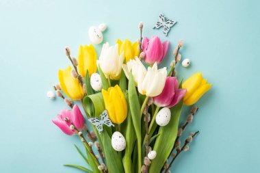 Easter decorations concept. Top view photo of bouquet of yellow pink white tulips pussy willow branches quail eggs and butterflies on isolated pastel blue background