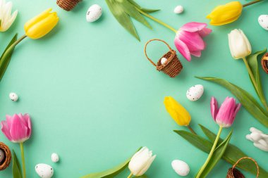 Paskalya konsepti. Küçük hasır sepetlerin, seramik paskalya tavşanı bıldırcın yumurtalarının ve izole edilmiş deniz mavisi arkaplanındaki renkli lalelerin ortasındaki telif boşluğunun en üstteki fotoğrafı.