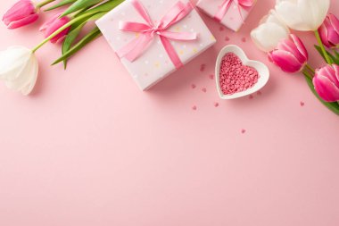 Anneler Günü konsepti. Üstünde pembe ve beyaz lale demetleri olan hediye kutuları ve izole edilmiş pastel arkaplan üzerine serpiştirilmiş kalp şeklindeki çay tabağı.