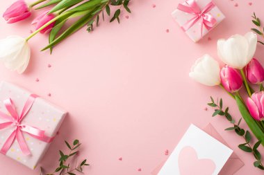 Mother's Day concept. Top view photo of gift boxes with bows bouquets of tulips envelope with postcard and sprinkles on isolated pastel pink background with blank space in the middle clipart