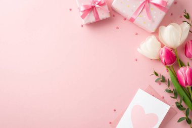 Anneler Günü konsepti. Hediye kutularının en üstteki fotoğrafında kurdele demetinde pembe ve beyaz lale zarfları var. Kartpostal ve kalp şeklinde zarflar, izole edilmiş pastel pembe arka planda, kopyalanmış pembe renkler serpiştirilmiş.