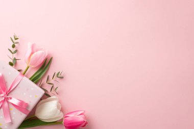 Anneler Günü konsepti. Üstten görünüşlü şık pembe hediye kutusu kurdele yayı ve izole edilmiş pastel pembe arka planlı lale buketi.