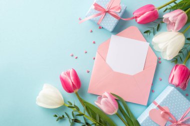 Anneler Günü konsepti. Zarfın üst görüntüsü, içinde mektup kutuları bulunan pembe beyaz laleler ve izole edilmiş pastel mavi arkaplan üzerine kalp şeklinde serpiştirilmiş boş alanlar.