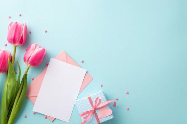 Anneler Günü kutlaması konsepti. Pembe lale buketinin en üst görüntüsü küçük mavi hediye kutusu, yay zarf kağıtları ve izole edilmiş pastel mavi arka plan üzerine serpiştirmeler.