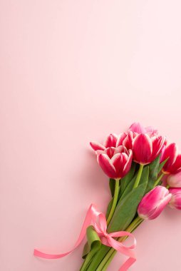 Anneler Günü konsepti. İzole edilmiş pastel pembe arka planda saten kurdeleyle bağlanmış lale buketinin dikey fotoğrafı