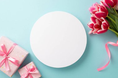 Anneler Günü atmosfer konsepti. Beyaz daire fotoğrafında pembe laleler ve pembe hediye kutuları var. Kurdeleli ve kopyalanmış pastel mavi arka planda.