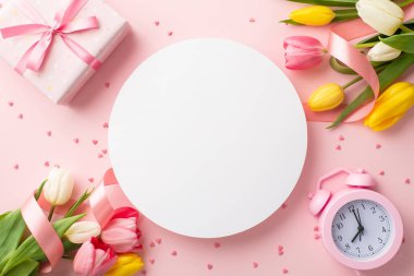 8 Mart konsepti. Renkli lalelerden oluşan beyaz daire buketlerinin üst görüntüsü. Kurdele hediye kutusu alarm saati ve kopyalanmış pastel pembe arka plan üzerine serpiştirilmiş.
