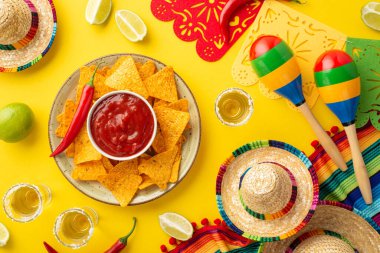 Cinco-de-mayonez konsepti. Geleneksel nacho cipsi kasesinin üst görüntüsü salsa soslu tekila ile tuz limonlu sombrero renkli serape çelenk marakaları izole edilmiş sarı arka planda.