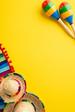 Cinco-de-mayonez konsepti. Meksika geleneksel şapkalarının dikey üst görüntüsü sombrero renkli seraplar ve izole edilmiş sarı arka plan üzerinde marakalar.