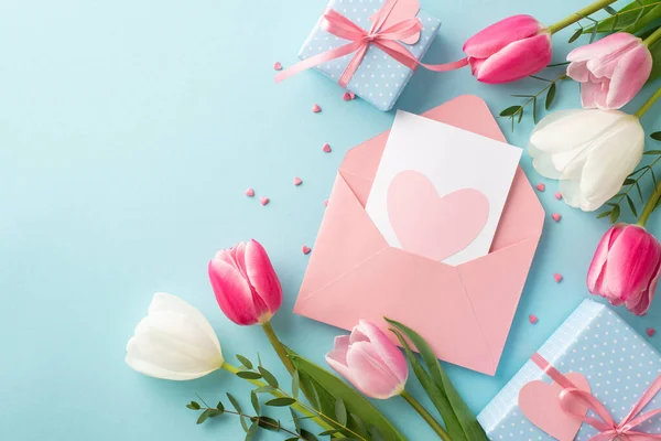 stock image Mother's Day concept. Top view photo of open envelope with postcard gift boxes with bows pink white tulips and heart shaped sprinkles on isolated pastel blue background