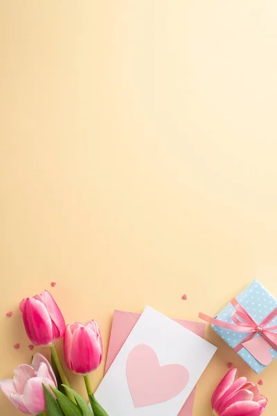 stock image Mother's Day concept. Top view vertical photo of bouquet of pink tulips blue giftbox with bow envelope with postcard and heart shaped sprinkles on isolated pastel beige background with copyspace