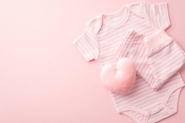 Bebek konsepti. Bebek kıyafetlerinin, pembe tulumların ve yumuşak kalp şeklinde oyuncakların izole edilmiş pastel pembe arka planda boş alanlarda çekilmiş en iyi fotoğrafı.